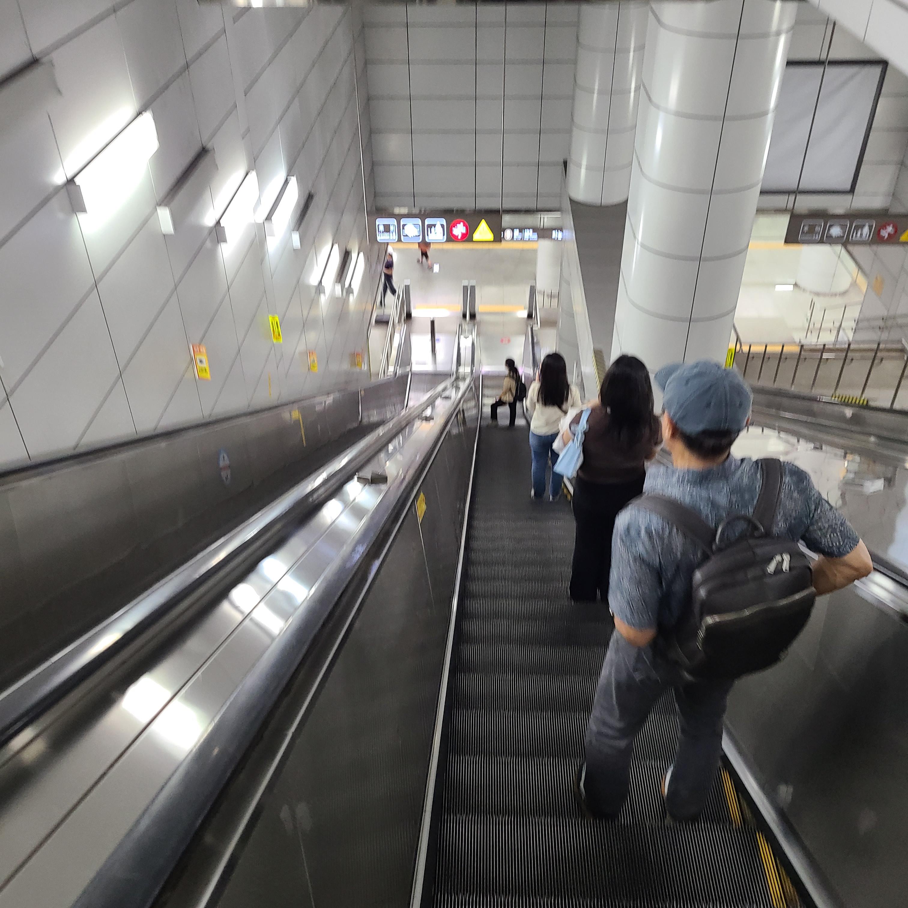 깊은 에스컬레이터를 타고 내려가는 사람들의 뒷모습 사진