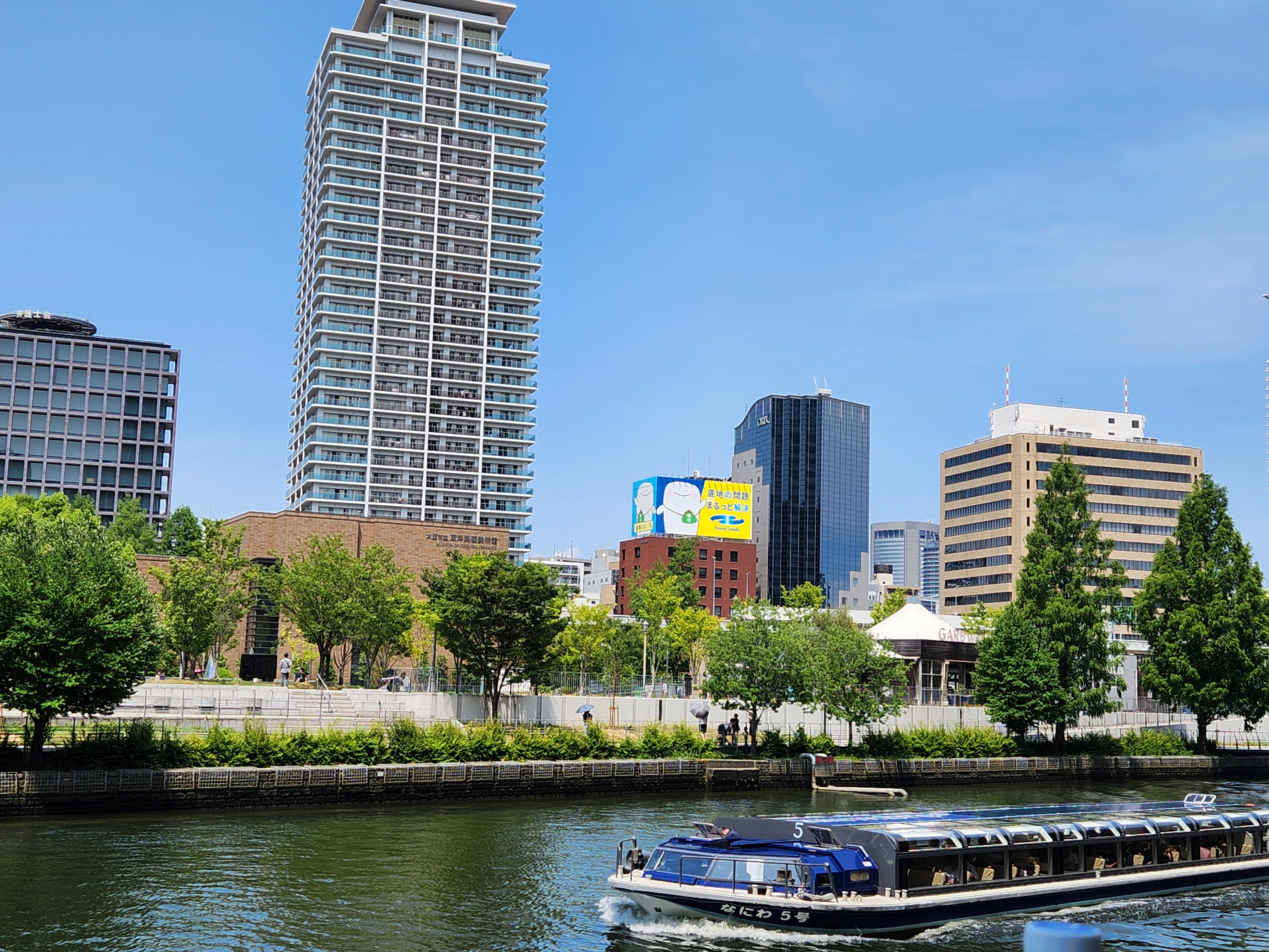 강 위를 천천히 지나가는 유람선과 오사카 중앙공회당이 보이는 강변 풍경