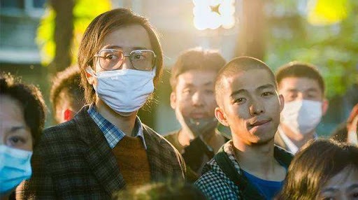 영화 《나는 약신이 아니다》에서 주인공이 마스크를 쓴 채 군중 속에 서 있는 장면. 이 장면은 병을 앓는 사람들과 그들의 삶을 대신 짊어진 자의 무거운 책임감을 강하게 전달한다.