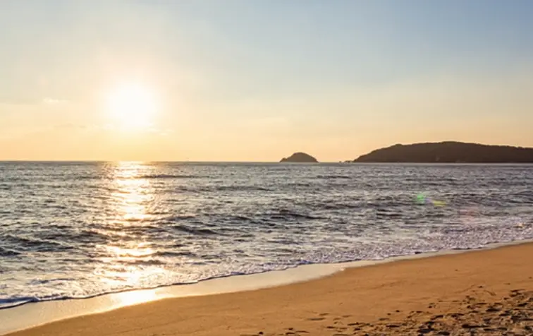 겨울방학 국내 여행지- 해가 지는 광경 앞 파도치는 바다와 노란 모래사장