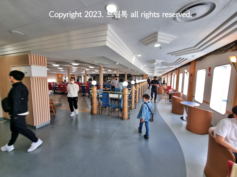 식당을 넓게 본 사진으로 많은 좌석에 사람이 앉아있고 이동하고 있다