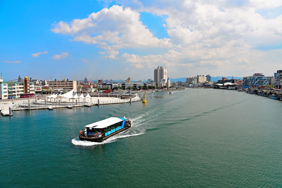 A small passenger boat on Pohang Canal, with the city and the steel mill skyline on both banks