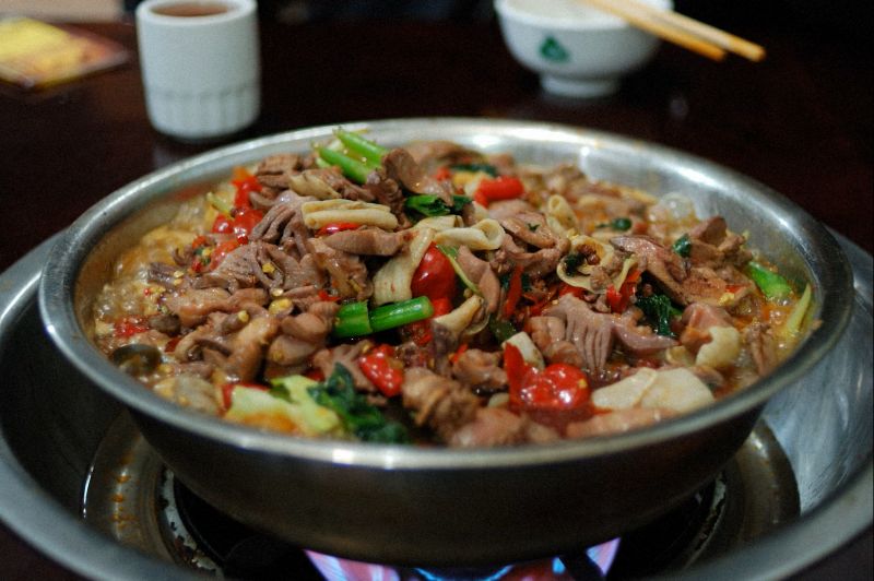 칭다오 식당에서 고추와 부추, 각종 내장 재료를 넣고 자작하게 끓여낸 매콤한 곱창볶음 요리, 불 위에서 따뜻하게 데워지며 향이 퍼지는 현지식 전골 스타일의 음식으로 현지인들이 즐겨 찾는 저녁 메뉴 분위기