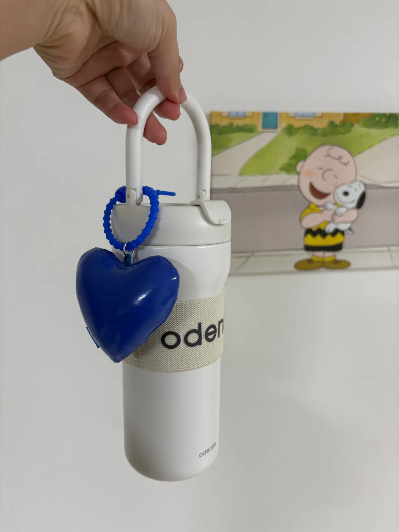 하얀-텀블러를-들고있는-손-텀블러에는-파란-하트-키링-뒤에는-아이와-강아지-그림