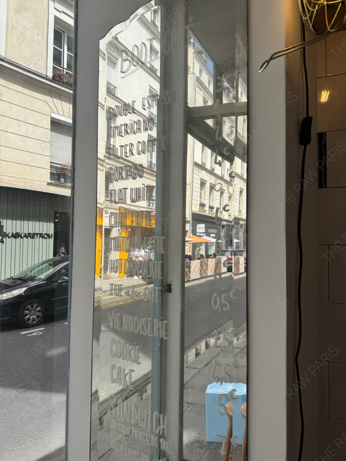 The menu written on the glass window of Boot Cafe Paris reflecting the street view ❘ Le menu écrit sur la vitre du Boot Café à Paris