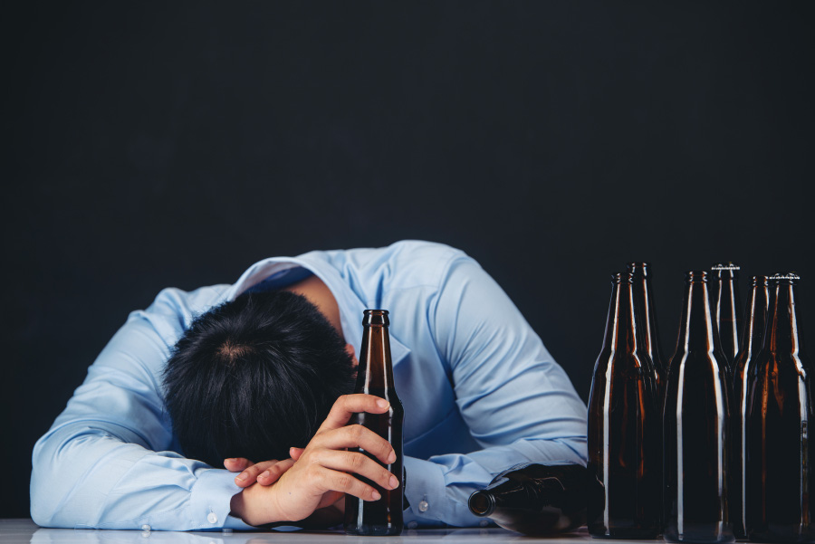 동양의 젊은 남성이 테이블 위에 다 마신 맥주병 6개와 손에 1병을 쥐고 엎드려서 술기운에 엎드려서 자고 있는 것을 찍은 사진