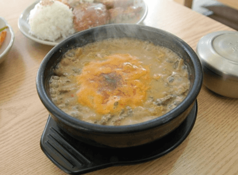 식탁 위에 미꾸라지로 만든 추어탕이 보글보글 끓고 있고 옆에는 돈가스가 있는 접시랑, 밥이 담긴 쇠밥 그릇이 있다.