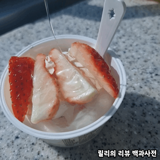 그릭요거트 위에 세로로 4등분 한 딸기를 올리고 꿀을 뿌리는 사진