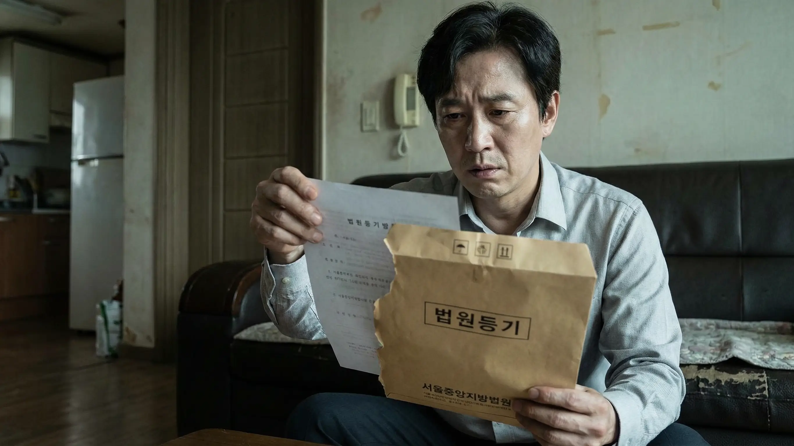 법원에서 온 등기 우편물을 손에 들고 불안해하며 내용을 확인하는 사람의 모습