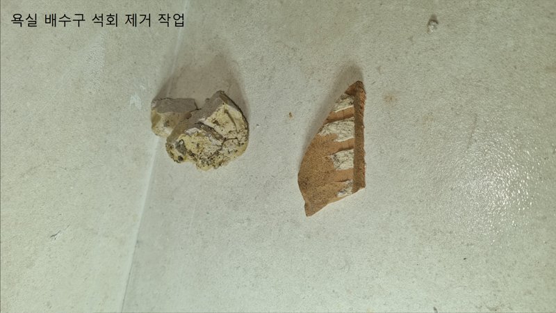 청담동 욕실 배수구에서 제거된 굳은 석회 조각을 바닥에 놓고 촬영한 실제 사진
