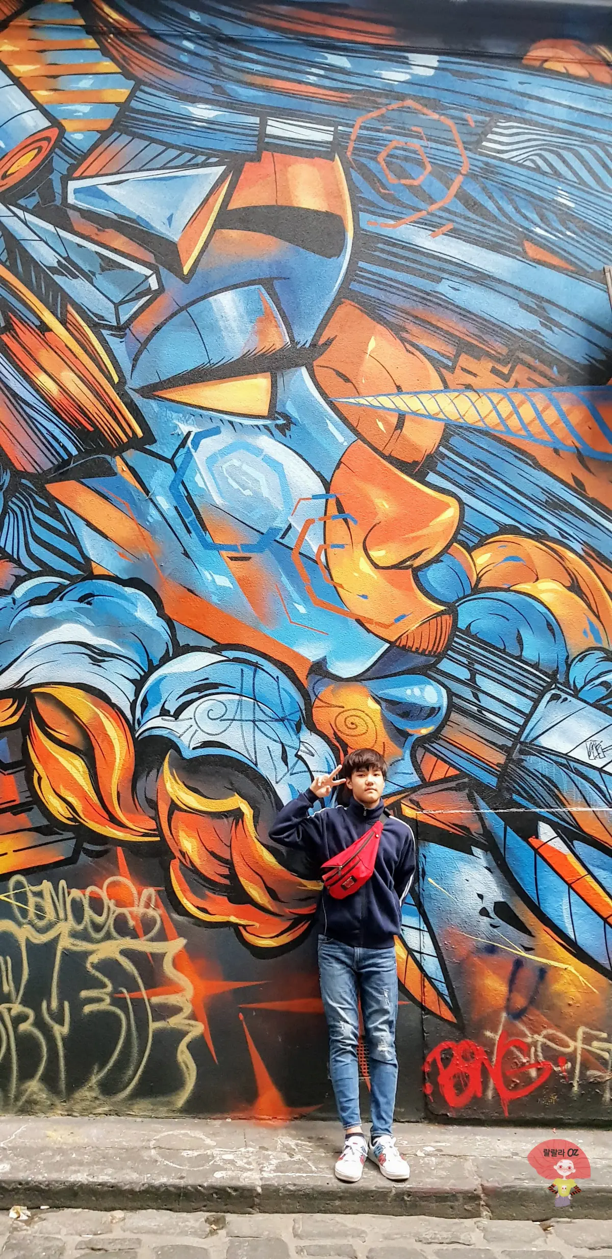 호주-멜버른-호시어-레인-거리-물마시는-여인의-알록달록한-거대한-얼굴을-담은-그래피티-앞에서-포즈를-취하는-소년