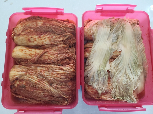 김치통에 가득 담긴 김장김치와 그위를 덮고있는 배추 겉잎