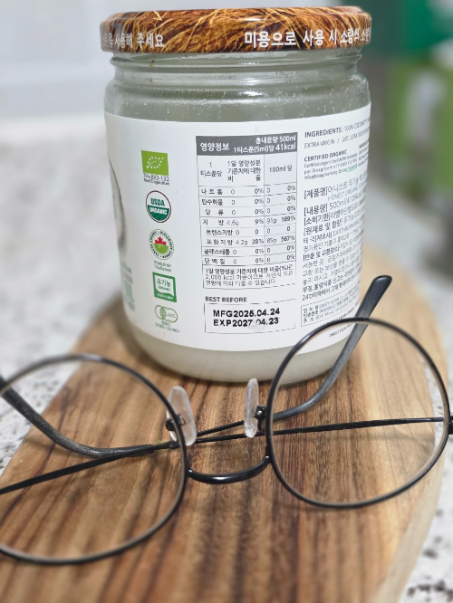 나무 도마 위에 놓인 코코넛 오일 성분표와 그 앞의 돋보기안경