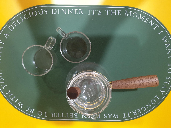 헌터색 테이블 매트 위에 유리 다관 및 찻잔 2개가 놓여있다. 항공샷으로 찍힘