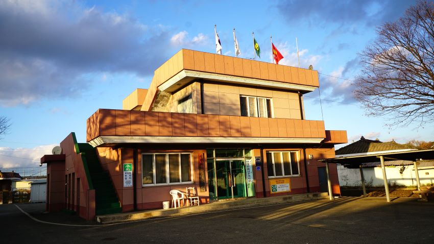 노란 2층 건물의 마을회관, 옥상에 태극기, 새마을기 포함 국기봉 4개, 푸른 하늘, 흰구름,