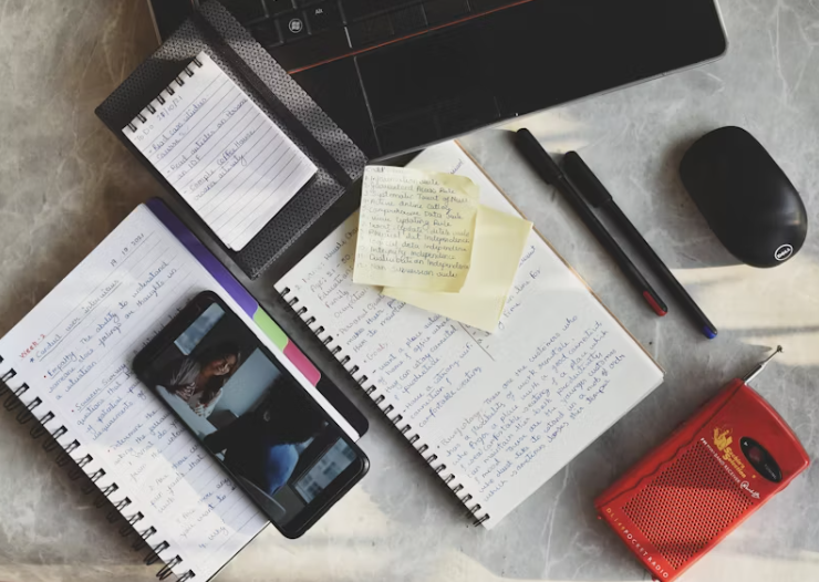 노트북, 수첩, 포스트잇, 펜, 스마트폰이 책상 위에 놓여 있고, 세법 관련 공부나 업무 준비를 하고 있는 듯한 장면