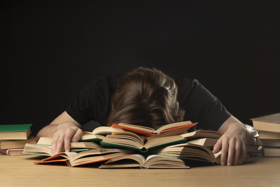 젊은 학생이 책상에 앉아서 책일 잔뜩 펼쳐 놓고 그 책 위로 머리를 박고 괴로워 하고 있는 것을 찍은 사진