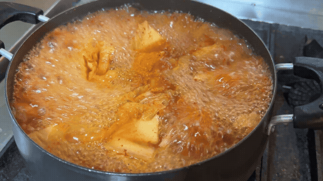 보글보글 끓고 있는 찌개 냄비. 김치와 오징어가 국물 속에서 어우러지며 매콤한 향이 전해지는 듯하다.