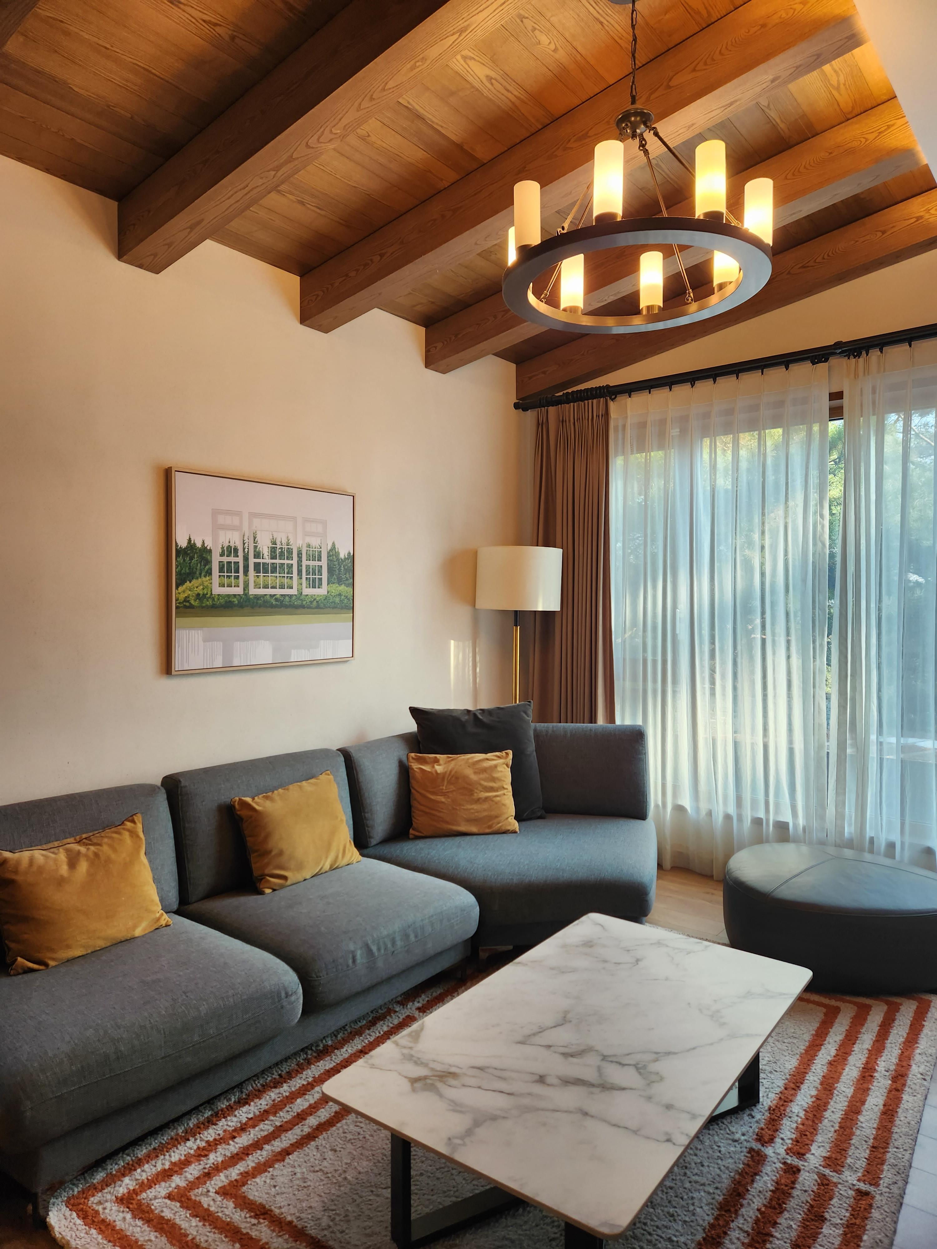 거실-나무로 된 천장-천장 조명은 원형 캔들로 은은한 빛을 내고 있음-짙은 파란색의 페브릭 소파와-컬러풀한 쿠션