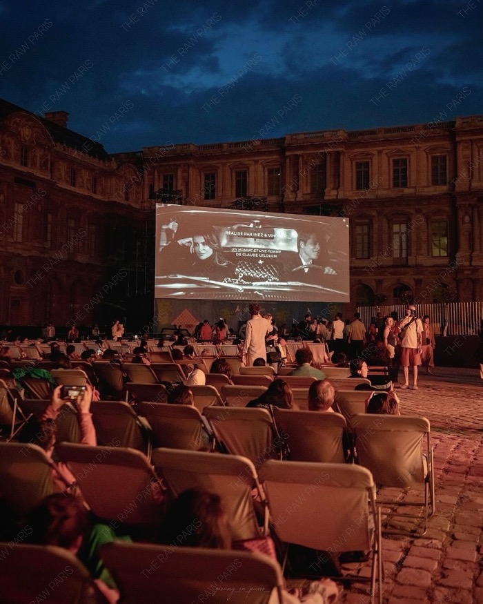 A crowded open-air cinema audience on deckchairs in front of a giant screen at the Louvre Museum during the Cinema Paradiso event