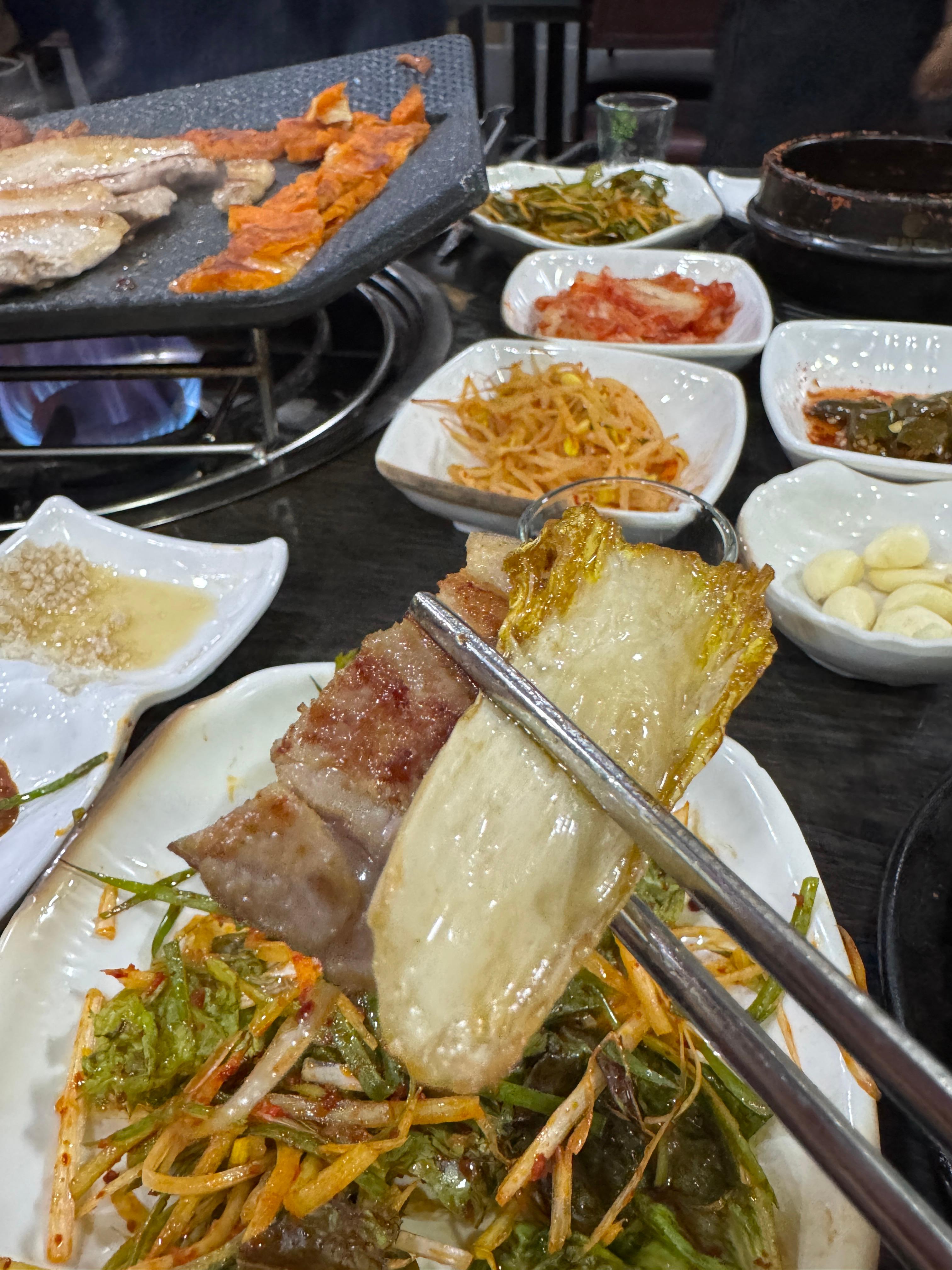 젓가락으로 구운 제주 오겹살과 백김치를 함께 집어든 모습.