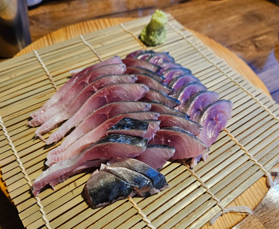 바다에서 채취를 한 고등어를 깨끗하게 손질한 후에 회를 쳐 놓은 것을 나무 테이블 위에 대나무 깔판을 깔고 그 위에 와사비와 함께 수북하게 놓아두고 찍은 사진