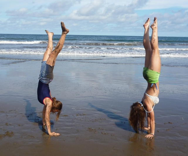 여성 2명이 바닷가에서 물구나무서기를 하고 있다.