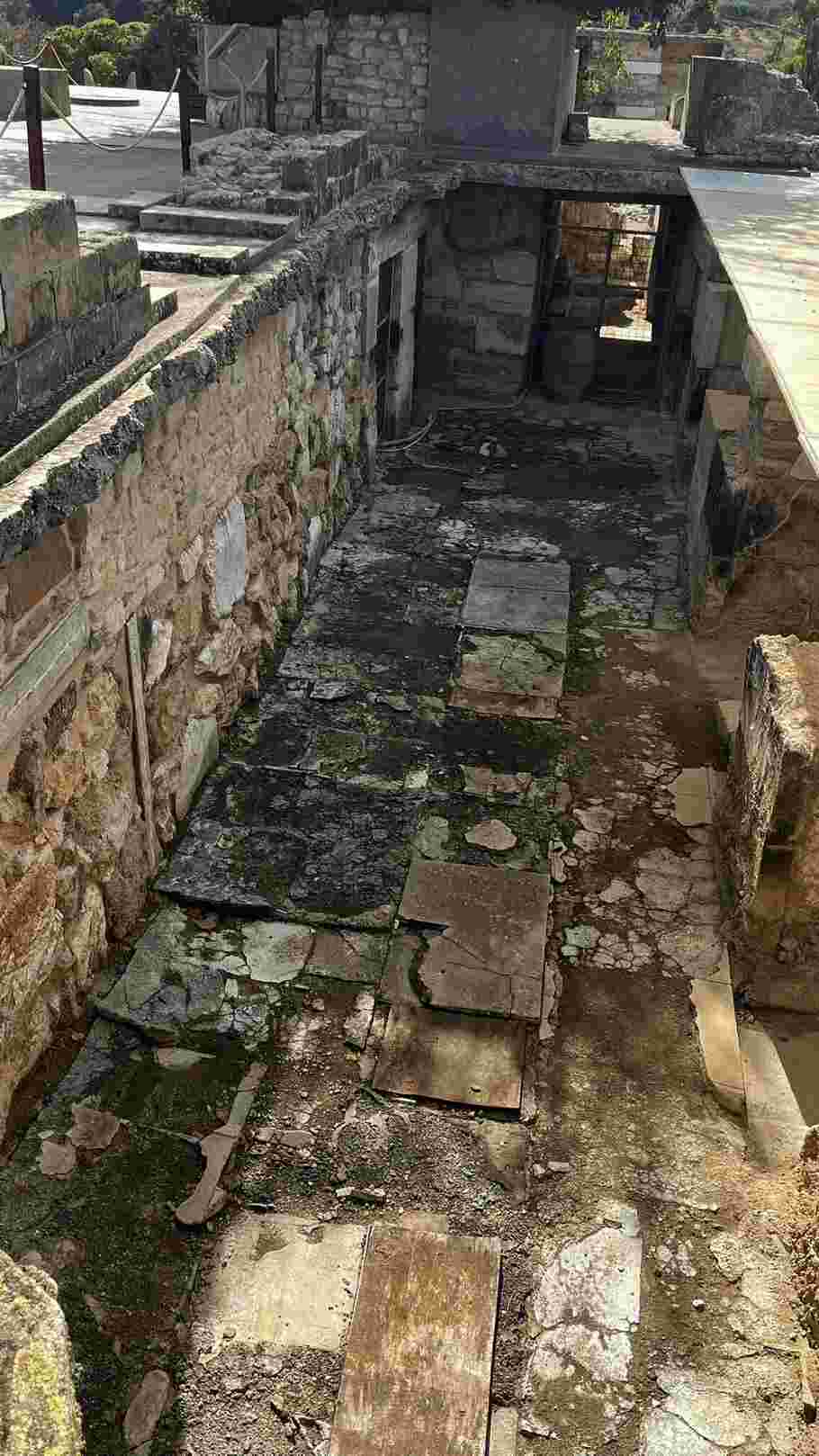 크노소스 궁전 하부의 석조 통로. 바닥에 판석과 배수 흔적이 있으며, 석조 벽으로 둘어싸인 구조물이다.