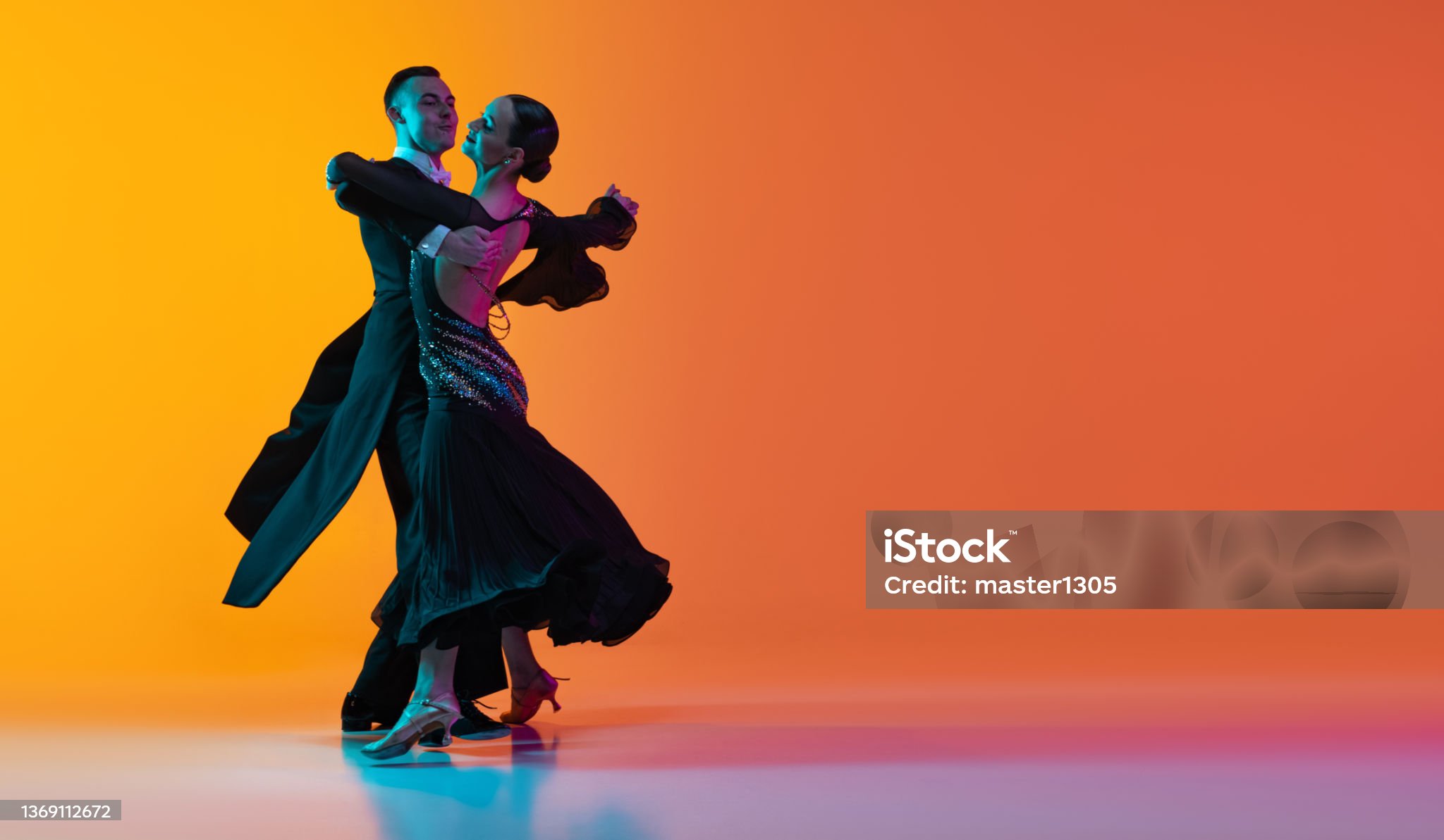 남여 한쌍이 정장과 등이파인 여자 드레스를 입고 손을 맞잡고 춤을추고 있는 사진입니다.