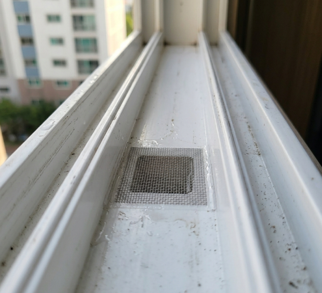 아파트 창틀 물구멍을 전용 방충망 스티커로 막아둔 모습