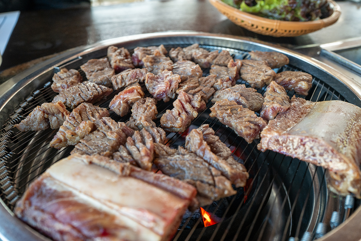 불판 위에서 갈비가 구워지고 있는 모습을 50mm 렌즈로 담아낸 모습. 불판 위 먹음직스럽게 구워지는 갈비의 질감이 잘 표현되어 있다
