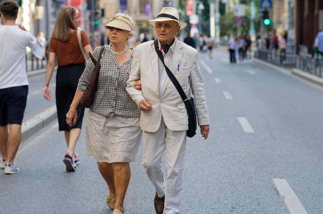 도심 거리에서 팔짱을 끼고 함께 걷는 노부부