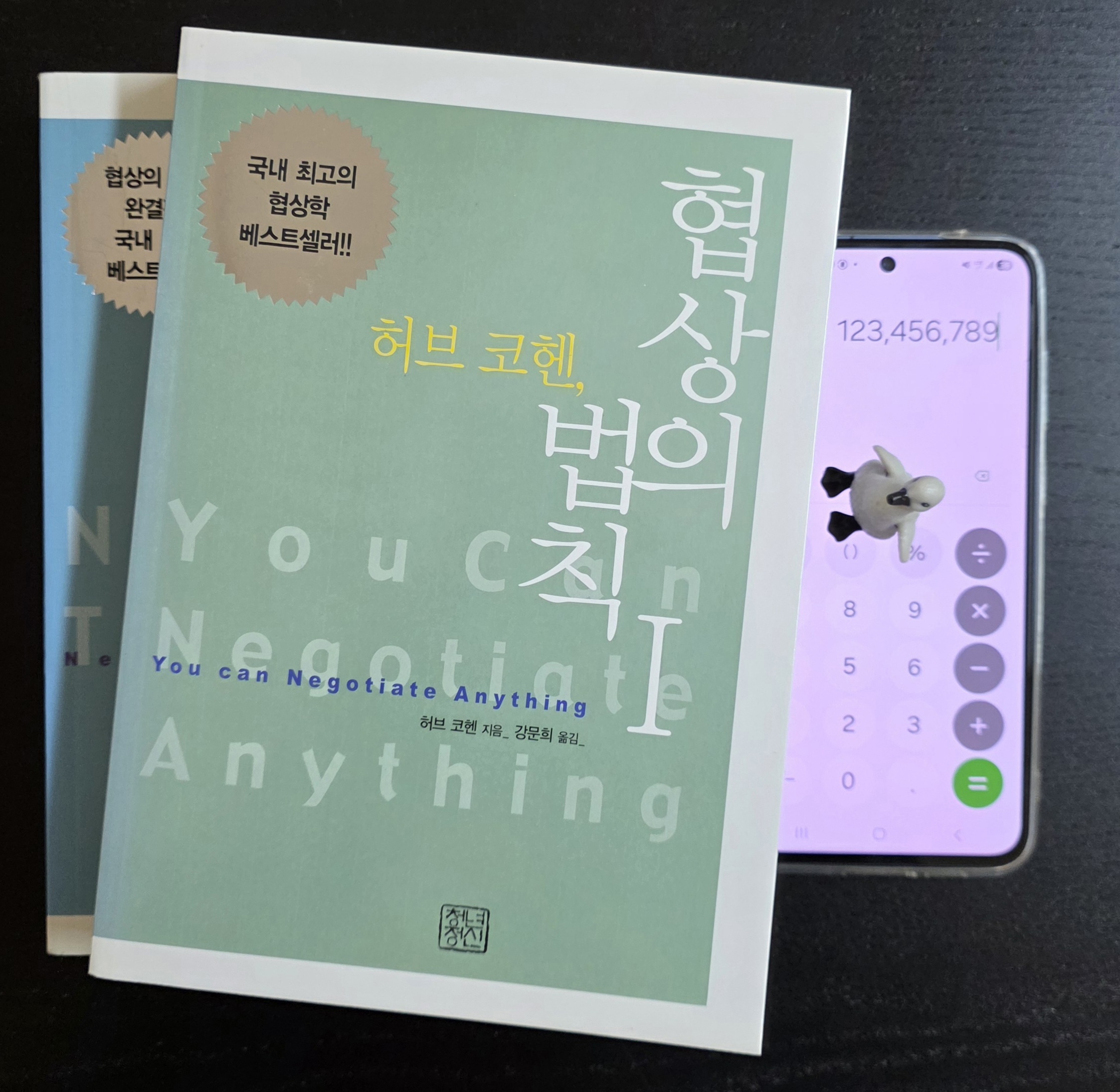 계산기 화면과 펭귄 피규어가 놓인 허브 코헨 협상의 법칙 책 표지