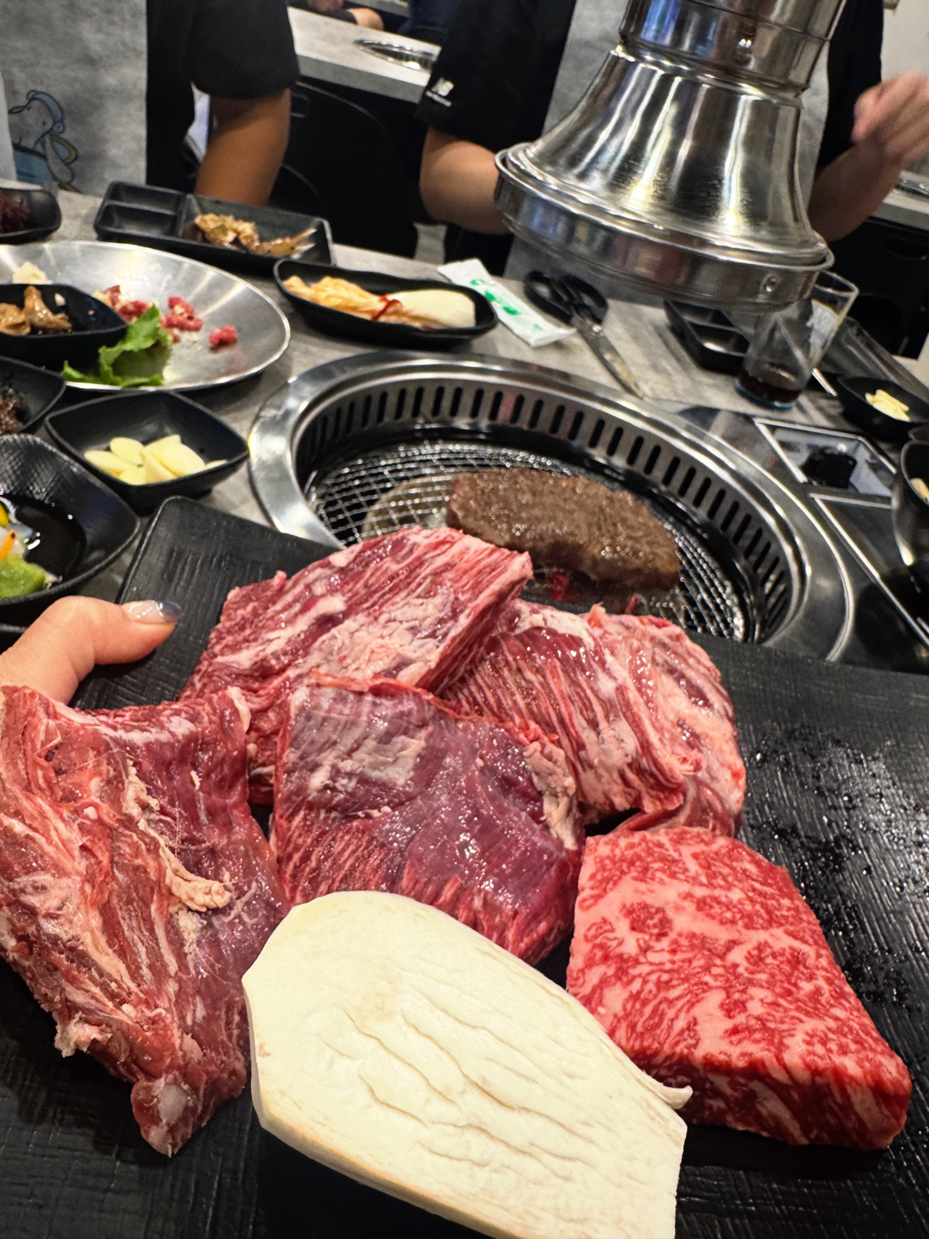 삼거리 명품한우에서 주문한 소고기 부위들. 새우살&amp;#44; 부채살&amp;#44; 살치살 등이 큼직한 상태로 접시에 담겨 있고 숯불 위에 고기가 익고 있는 모습이 보인다.