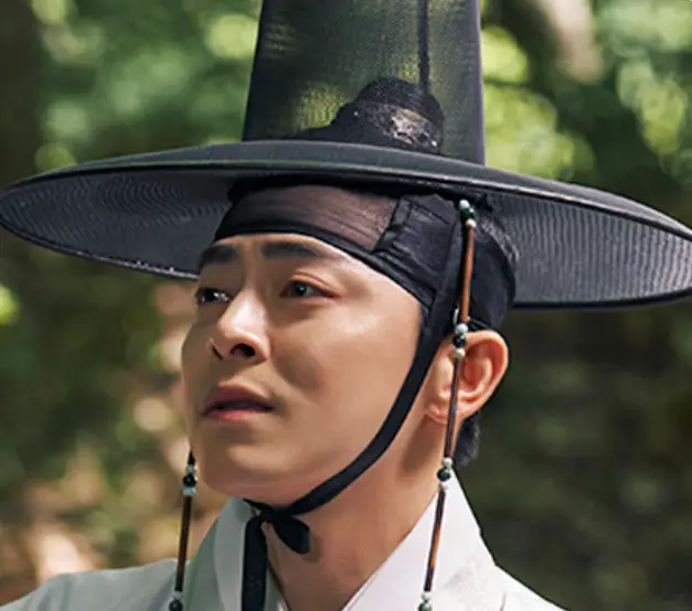 세작- 갓을 쓰고 흰 도포를 입은 조정석이 숲에서 먼곳을 바라보는 모습