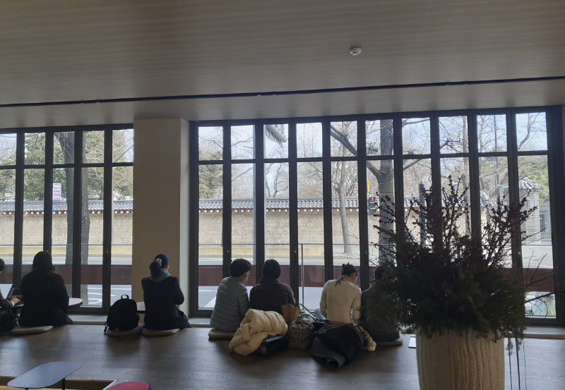 긴 폴딩창을 바라보며 좌석이 배치되어있다. 사람들은 경복궁 담을 보며 커피를 마시고 있다.