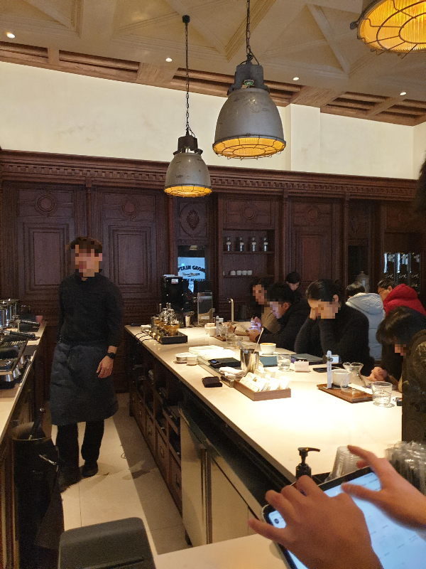 주문 받는 코너와 바리스타 추출공간이 붙어 있다. 바형 테이블에 손님들이 앉아 있다.