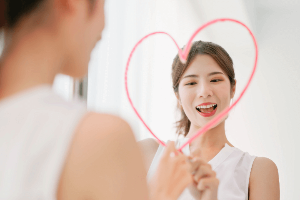 거울에 분홍색 색연필로 하트를 그리는 여자