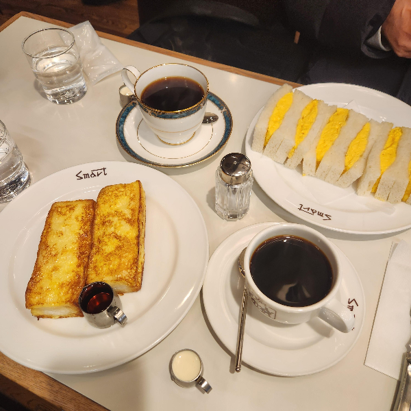 테이블위 커피 두잔과 계란 샌드위치 그리고 토스트가 놓여 있다.