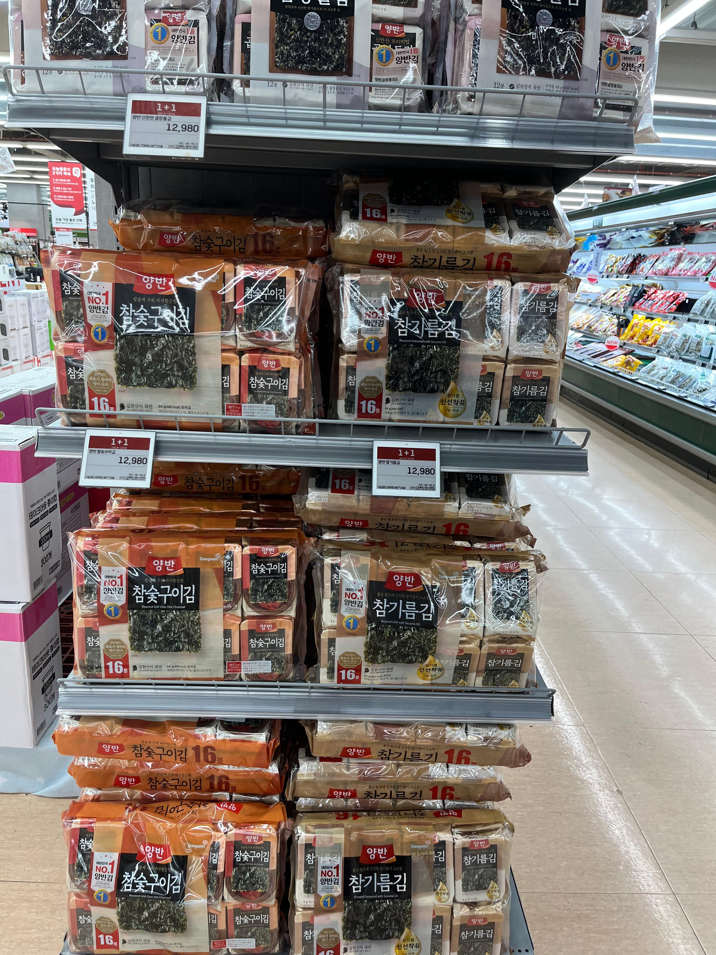 “Stacks of Korean roasted seaweed (gim) packs displayed in a supermarket aisle, featuring brands like Yangban’s sesame and charcoal-grilled varieties, sold as 1+1 deals in Korea.”