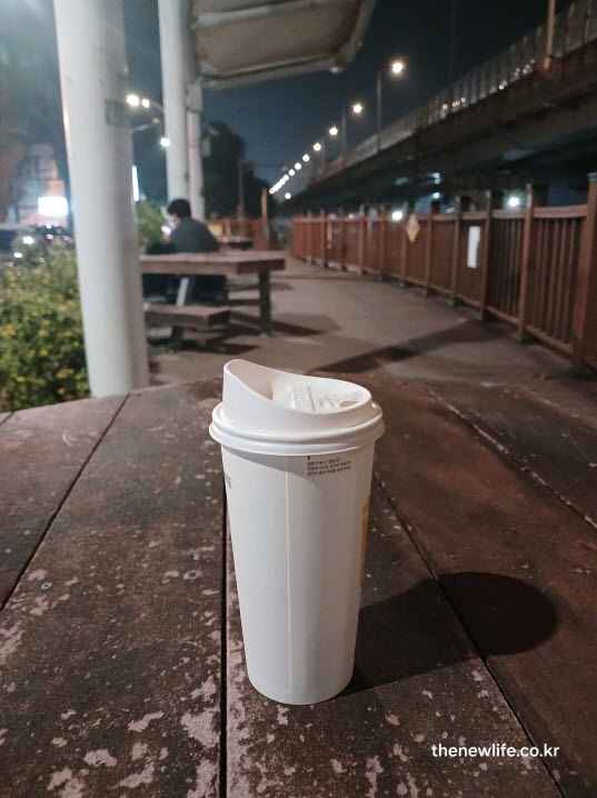 야간 산책 중 나무 테이블 위에 놓인 테이크아웃 블랙커피 컵