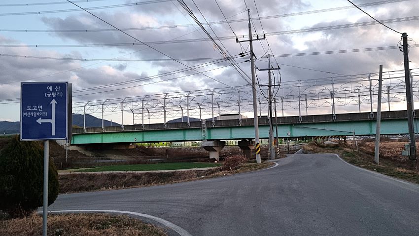 어두워지는 하늘에 회색 구름들, 좌우로 지자가는 교량, 계촌교, 삼거리 왼쪽에 진한 파란 바탕에 흰 화살표 표시된 이장표,