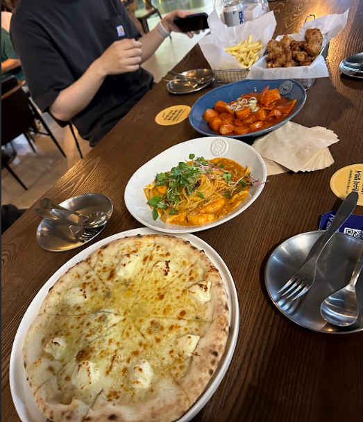 떡볶이, 파스타, 피자, 치킨 등 맛있는 음식들이 테이블 가운데에 모여있다.