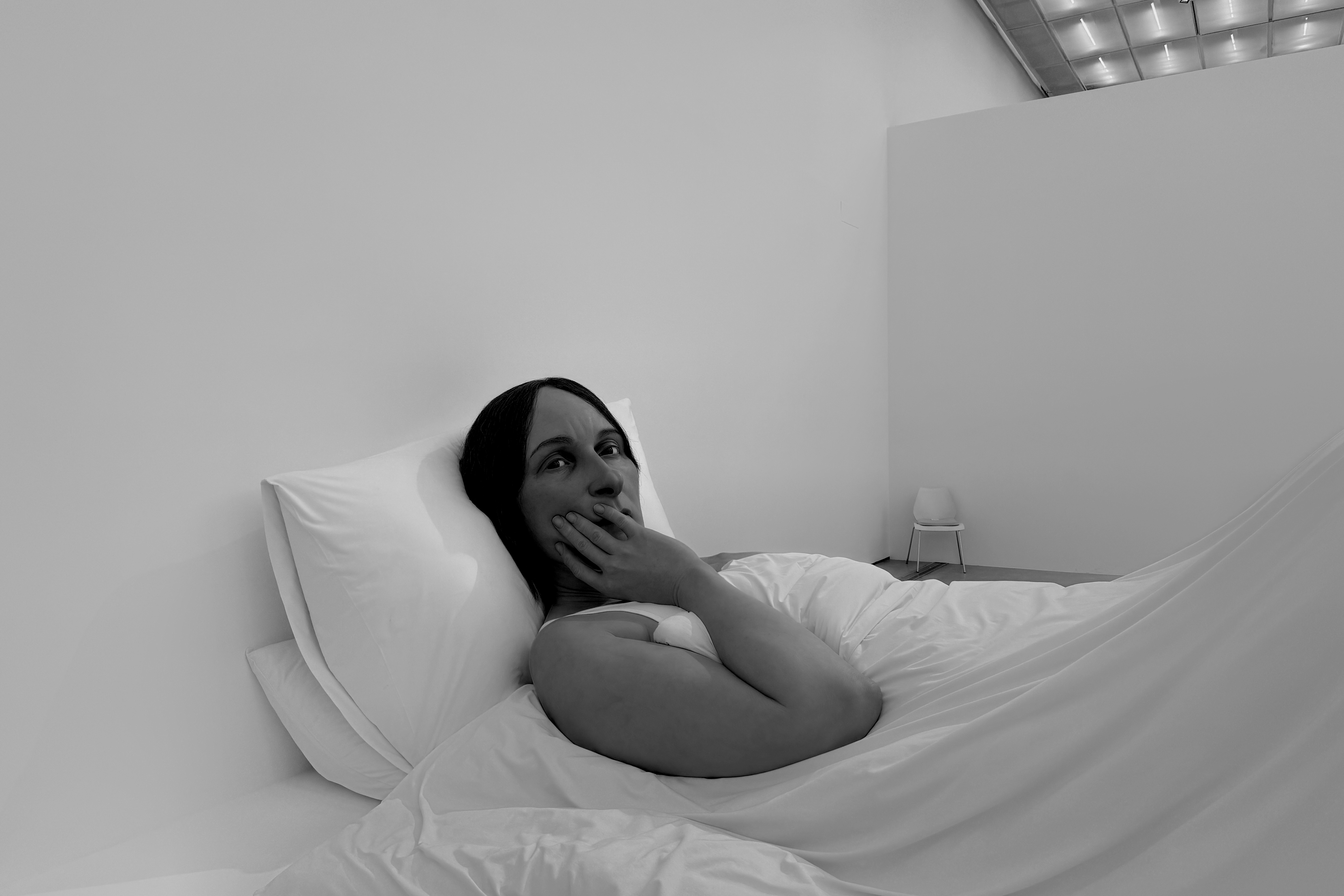 《침대에서》 작품 - 거대한 침대에 누워 한 손으로 입을 가리고 있는 여성의 조각. 하얀 침구와 베개가 섬세하게 표현되었으며, 인물의 표정과 자세에서 불안과 고독이 느껴집니다. 일상적 순간을 통해 깊은 감정을 전달합니다.