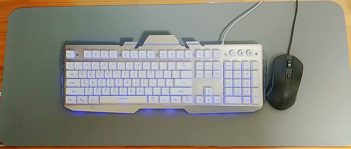 회색-장패드-위에-흰색-키에-파란색-불이-들어오는-은색-몸통의-키보드와-검은색-마우스가-있다