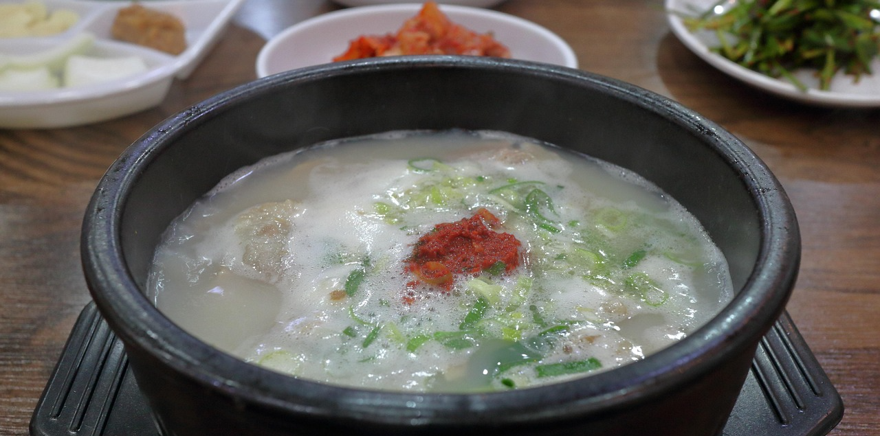 돼지국밥- 고추가루, 파가 들어 있는 국밥 한그릇과 반찬들의 모습.