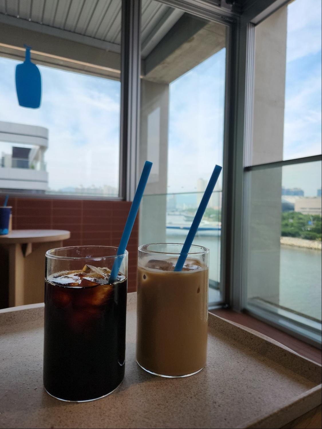 파란 빨대가 꽂힌 유리 잔 2개. 1잔에는 블랙커피가, 다른 1잔에는 밀크 커피가 담겨 있다