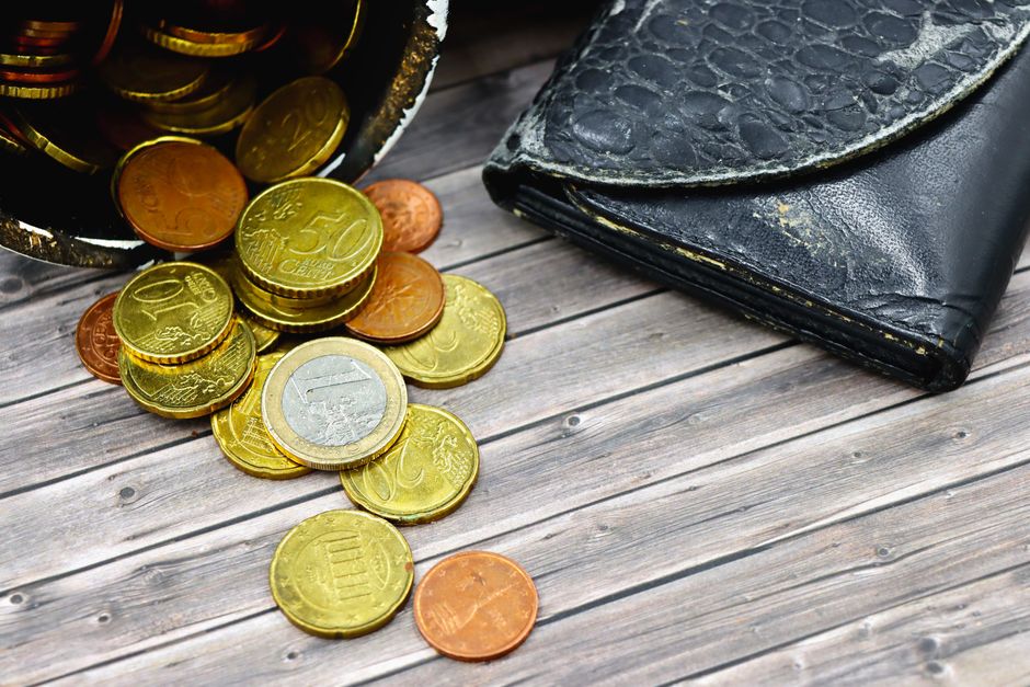 A worn-out leather wallet and scattered euro coins on wooden surface suggest economic hardship.