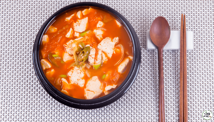 뚝배기에 순두부찌개가 담겨있고 옆으로 나무수저가 놓여져 있다