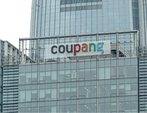 고층 빌딩 상단에 선명하게 부착된 'coupang' 브랜드 로고와 기업 외관 전경